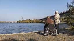 Mann im Rollstuhl mit älterem Pärchen am Flussufer mit Blick auf den Zusammenfluss von Saar und Mosel
