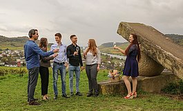 Gruppe junger Menschen beim Anstoßen neben einer Steinskulptur, Blick auf das Moseltal